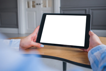 Over shoulder closeup view: woman hands holding digital tablet computer device with white blank screen in home interior. Mock up, copyspace, template, entertainment and technology concept