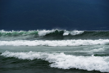 Stormy sea view near coastline against dark background. Waves and splashed drops.