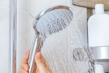 Woman hand using shower head in bathroom. - obrazy, fototapety, plakaty