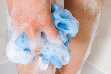 Woman with sponge washing legs in bathroom.