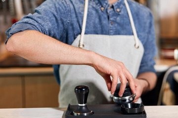 Hands of barman opening cover of tamper, holds pot of tamper with fingers in modern coffee house, blurred background