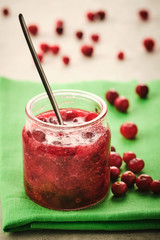 Cranberry jam in a glass bowl with fresh berries close-up.