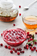 Cranberry jam in a glass bowl and teapot on a white background.