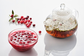 Cranberry jam in a glass bowl and teapot on a white background.