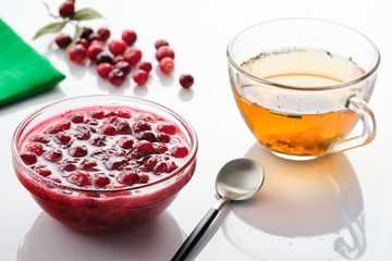 Cranberry jam in a glass bowl and teapot on a white background.