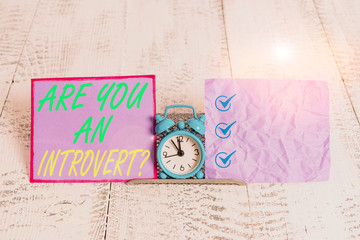 Text sign showing Are You An Introvertquestion. Business photo text demonstrating who tends to turn inward mentally Mini blue alarm clock standing above buffer wire between two notation paper