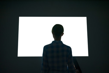 Woman silhouette looking at white blank interactive wall display in dark room of modern technology...