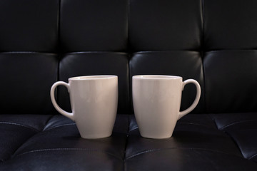 Two coffee cups placed on the black sofa