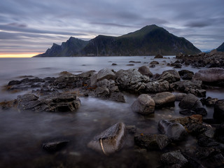 Waves flow over rocks on a rocky beach after sunset