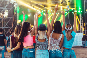 Back view of group of female friends at music festival drinking beer and dancing	