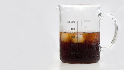Black coffee with cube ice in glass jug have scale for volume in white background.