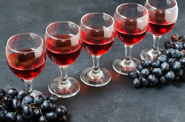 Red wine in glasses, a bunch of black grapes. Dark background.