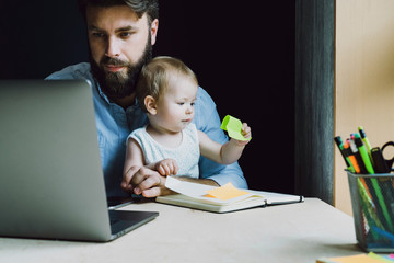 Baby sitting on knees of working parent. Father doing work at home sending projects online. Dad...