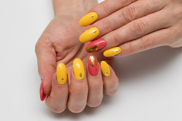 Autumn yellow, orange, coral manicure on long oval nails with crystals, rhombuses and a gold falny on a white background close-up. 