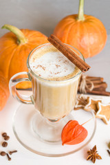 Pumpkin latte with cinnamon in a glass on a gray background. Pumpkins, coffee, spices and cookies. Side view, close-up, copy space. Selective focus.