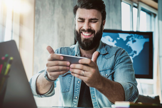 Digital specialist at office desk using mobile phone for social media communication. Guy watching funny videos on smartphone