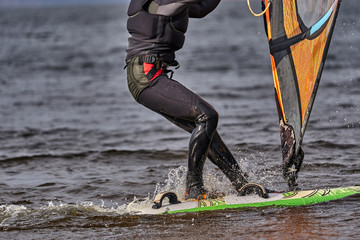A male athlete is interested in windsurfing. He moves on a Sailboard on a large lake on an autumn...