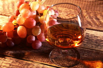 Cognac or Brandy in a glass and fresh grapes, still life in rustic style, vintage wooden background, selective focus.