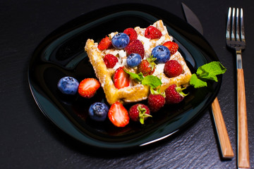 Belgian waffles with raspberries, strawberries and blueberries on a black plate. Selective focus.