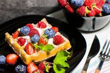 Belgian waffles with raspberries, strawberries and blueberries on a black plate. Selective focus.