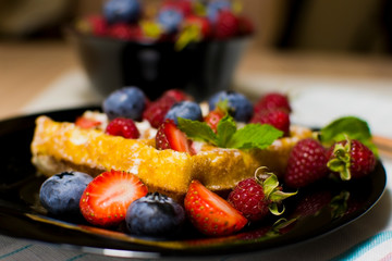 Belgian waffles with raspberries, strawberries and blueberries on a black plate. Selective focus.