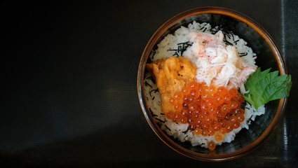 a bowl of rice with sashimi on top. or kaisendon sashimi donburi which have fresh ikura (salmon roe), uni, giant crab in the black bowl on black tray from top view