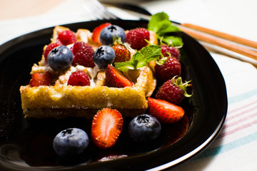Belgian waffles with raspberries, strawberries and blueberries on a black plate. Selective focus.