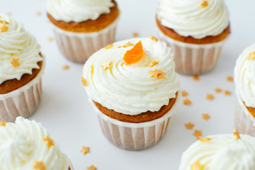 Group of cupcakses with cream, orange candied fruit and gold confectionery sprinkling at white table background. Picture for a menu or a confectionery catalog.