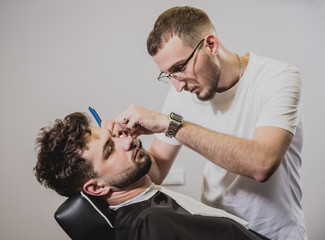 Young man with trendy haircut at barber shop. Barber does the hairstyle and beard trim.