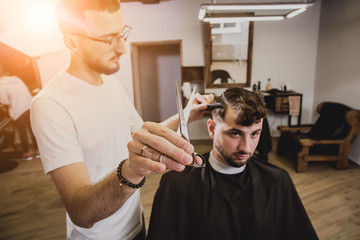 Young man with trendy haircut at barber shop. Barber does the hairstyle and beard trim.