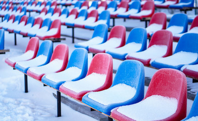 Snow-covered multi-colored seats in the stadium in winter. Snowfall interferes with sports....