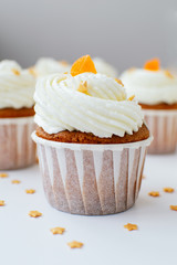 One cupcake with cream, orange candied fruit and gold confectionery sprinkling. Picture for a menu or a confectionery catalog.