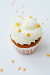 One cupcake with cream, gold confectionery sprinkling at white background. Picture for a menu or a confectionery catalog.
