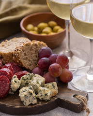 Charcuterie board with different snacks for wine. Blue cheese, olives, baguette slices, cured meat and grapes Wine snacks set background.