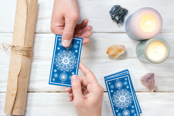 Tarot cards in fortune teller hand on white wooden table background. Future reading.