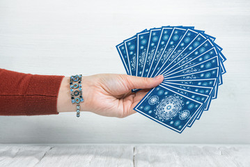 Tarot cards in fortune teller hand on white wooden table background. Future reading.