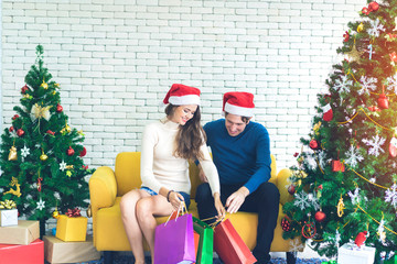 Young Caucasian couple going to buy present for Christmas gifts for family. Sitting on yellow couch to check each bags and count number of boxes with Christmas tree decoration at home, Happy new Year 
