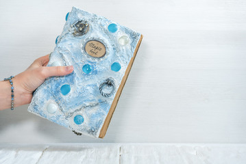 White magic book in a sorceress hand on a white wooden table background.
