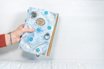 White magic book in a sorceress hand on a white wooden table background.