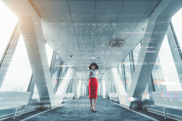 African-American woman entrepreneur is standing indoors of a long bright futuristic passageway of a skyscraper and using her smartphone surrounded by login and privacy check UI infographics