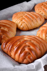 Yeast wicker buns with filling in the oven tray on the edge of the table against black background