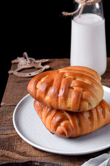 Yeast braided buns on a ceramic plate and a bottle of milk of the edge of the wooden table against black background