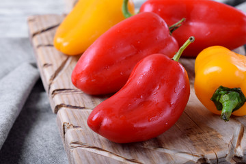 Little red and yellow bell peppers on wooden board