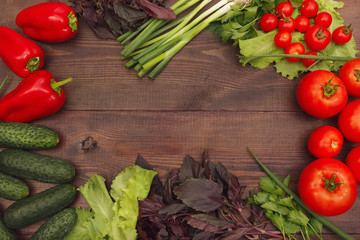 Tomatoes, cucumbers, bellpeppers, lettuce, basil and leek on a wooden table. View from above.