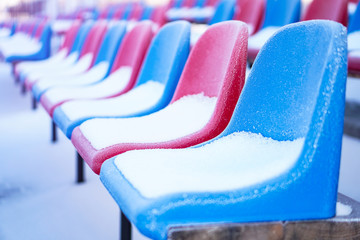 Snow-covered multi-colored seats in the stadium in winter. Snowfall interferes with sports....