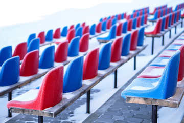 Snow-covered multi-colored seats in the stadium in winter. Snowfall interferes with sports....
