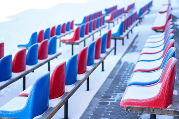 Snow-covered multi-colored seats in the stadium in winter. Snowfall interferes with sports....