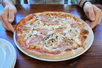 a man holds a whole big pizza on a plate. Italian cuisine, baked in the oven. delicious food in the restaurant, serving