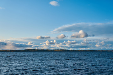 Blue waving water of a lake with autumn forest on horizon with cloudy sky on a background.