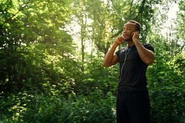 Runner standing and listening music in forest.